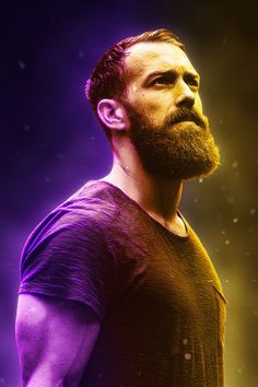 a man with a beard standing in front of a purple and yellow background, looking off to the side
