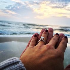 two hands holding each other on the beach with waves in the background and clouds in the sky