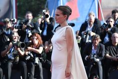 a woman in a white dress standing on a red carpet next to photographers and papas