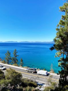 cars are parked on the side of the road by the water's edge, with mountains in the distance