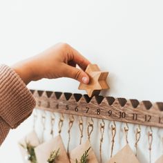 a person holding a wooden star on top of a ruler with christmas decorations hanging from it