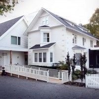 a large white house sitting on the side of a road next to a fence and trees