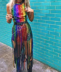 a woman standing in front of a blue brick wall wearing a rainbow colored fringe dress