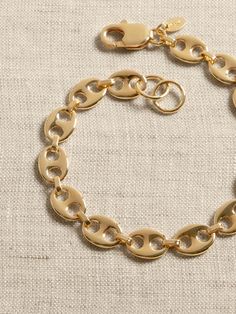 a gold chain bracelet with oval links on a white cloth covered surface, close up