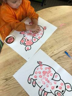 two children's drawings on white paper with pink dots and an orange shirt sitting at a table