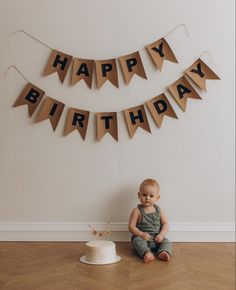 a baby sitting on the floor in front of a birthday cake and bunting banner