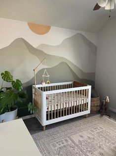 a baby's room with mountains painted on the wall and a crib in the corner