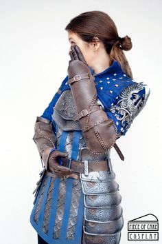 a woman dressed in armor and holding her hands to her face