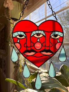 a stained glass heart hanging from a chain with eyes and tears attached to it
