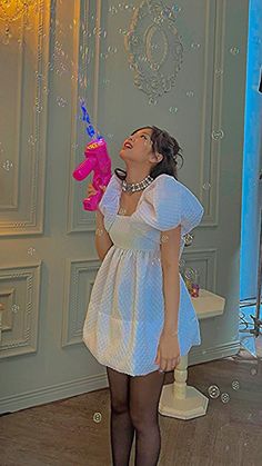 a woman in a white dress blowing bubbles with a pink teddy bear on her nose