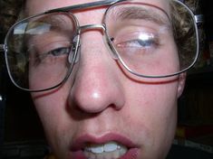 a close up of a person wearing glasses and making a face with his tongue out