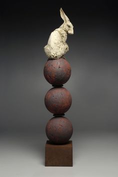 a sculpture of a rabbit sitting on top of three balls in front of a dark background
