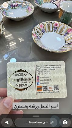 a person holding up a business card in front of many bowls and plates on a table
