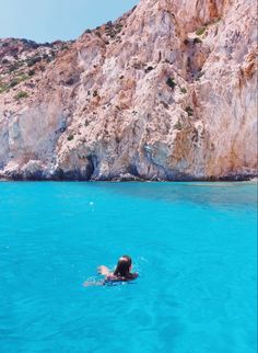 a person swimming in the blue water near a rocky cliff face and body of water