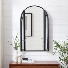 an arched mirror hangs on the wall above a wooden dresser with vases and plants