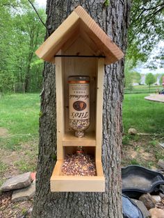 a wooden bird feeder hanging from a tree in the woods with a bottle of whiskey on it