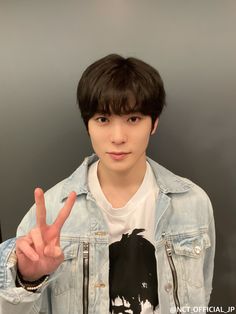 a young man making the peace sign with his hand while wearing a jean jacket and white t - shirt