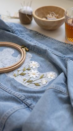 a denim jacket with embroidered flowers on it next to a glass of alcohol and other items