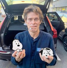 a man standing in front of a car holding two snoopy dog magnets on his fingers