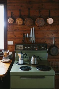 a green stove top oven sitting inside of a kitchen next to a wall with pots and pans on it