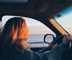 a woman driving a car near the ocean at sunset with her hands on the steering wheel