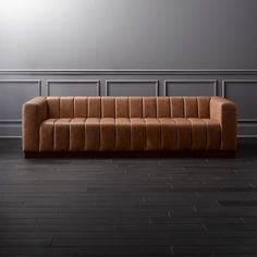 a brown couch sitting on top of a hard wood floor next to a gray wall