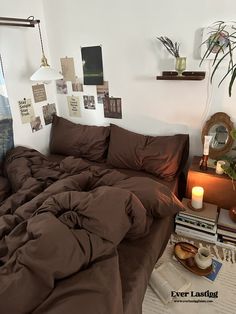 a bed with brown sheets and pillows in a bedroom next to a table with books