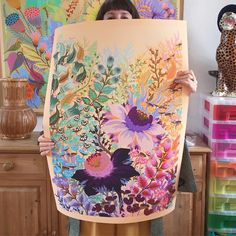 a woman holding up a large painting with flowers on it