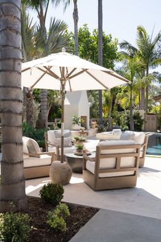 an outdoor patio with furniture and umbrellas near a swimming pool surrounded by palm trees