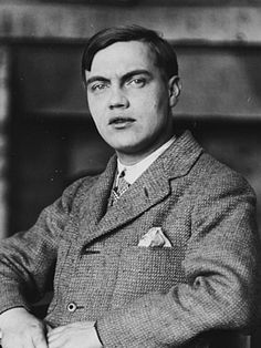 an old photo of a man in a suit and tie sitting at a table with his arms crossed