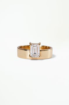 a gold ring with an emerald cut diamond in the center, on a white background