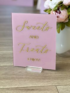 a pink sign that says sweets and treats enjoy with flowers in the background on a table