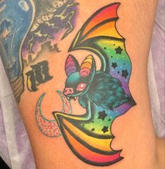 a colorful tattoo on the leg of a person with a bat and crescent moon design