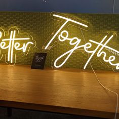 two neon signs sitting on top of a wooden table next to each other with the words together