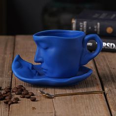 a blue coffee cup sitting on top of a wooden table next to some coffee beans