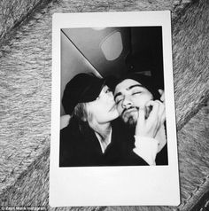 black and white photograph of two people kissing each other on the forehead, with one person wearing a beanie