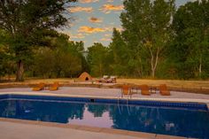 an empty swimming pool with lounge chairs around it and trees in the background at sunset