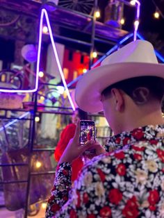 a woman wearing a cowboy hat taking a photo with her cell phone at night time