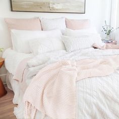 a white bed with pink comforter and pillows on top of it in a bedroom