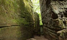 a narrow path between two large rocks with moss growing on them