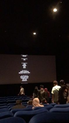 people are standing in front of a projection screen at an auditorium with blue velvet seats