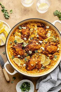 a pot filled with chicken and rice next to lemon wedges on top of a table