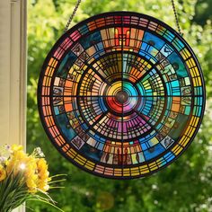 a stained glass sun catcher hanging on a window sill with flowers in the foreground