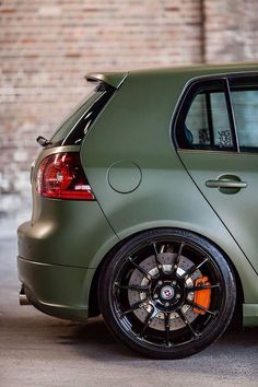 a green car parked in front of a brick wall with orange wheels and rims