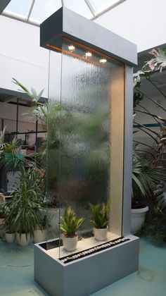 an indoor fountain with plants in it and lights on the top part of the water tank