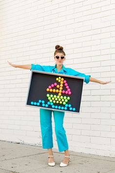 a woman in blue pants and sunglasses holding a sign with an image of a triangle