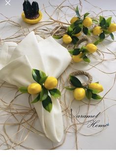 some yellow lemons and green leaves on a white table cloth with twine around them