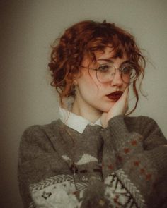 a woman with red hair wearing glasses and a sweater