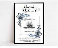 a wedding card with blue flowers and leaves on the front, in black frame against a white wall