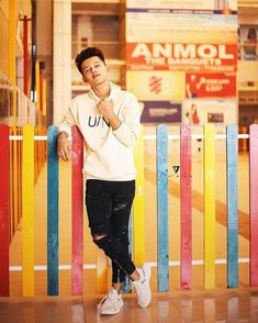 a young man leaning against a colorful fence with his hand on his chin and looking at the camera